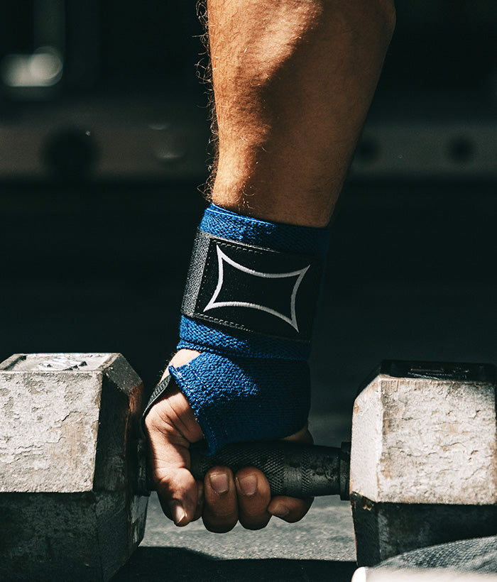 male wearing blue wrist wraps holding a dumbbell