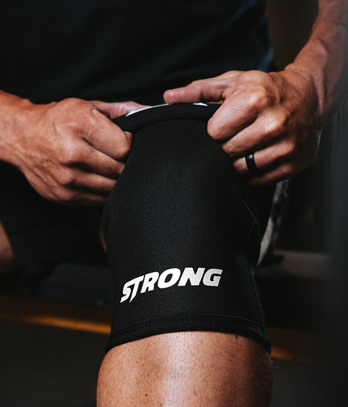 male putting on all black knee sleeves with the label strong on it